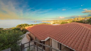 A coastal property with a red-tiled roof, a balcony, and a view of the sea and distant landscape. - Calypso Lux Independent Villa (AGLIENTU)