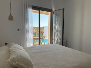 A bedroom with a large bed, a view of a pool and outdoor seating, and a sliding glass door. - 2-bedroom villa Odysseus (Antiparos)