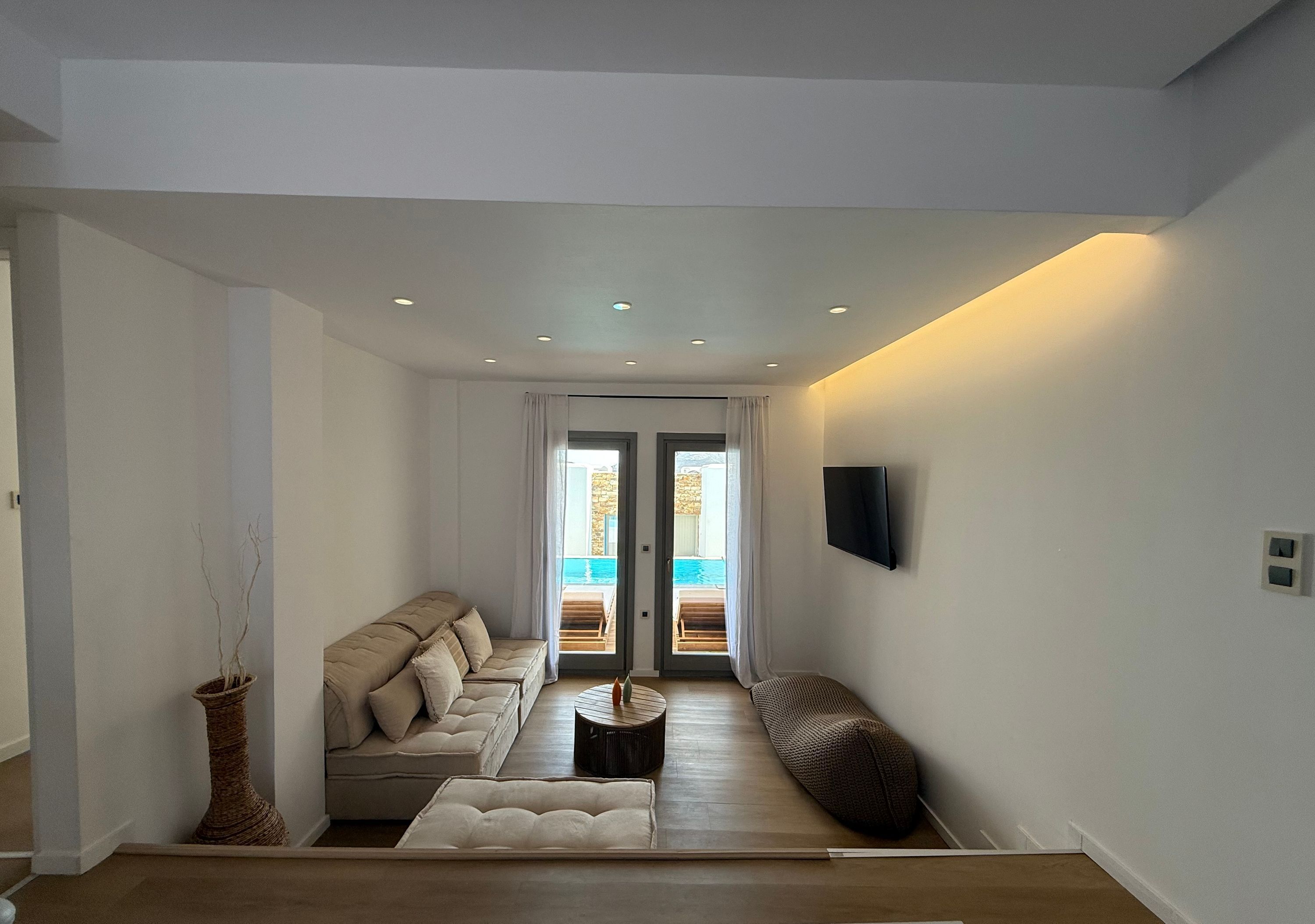 Un salon moderne avec un canapé, une table basse et une vue sur une piscine extérieure, visible à travers une porte vitrée.