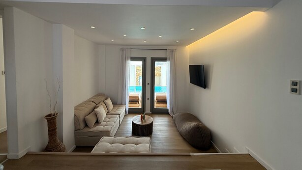 Uma sala de estar moderna com um sofá, uma mesa de centro e vista para uma piscina ao ar livre por uma porta de vidro.