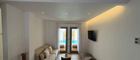A modern living room with a sofa, a coffee table, and a view of an outdoor swimming pool through a glass door.
