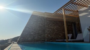 Uma área à beira da piscina com muro de pedra, pérgola de madeira e espreguiçadeiras.