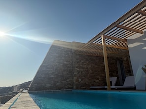 A poolside area with a stone wall, wooden pergola, and lounge chairs. - 2-bedroom villa Odysseus (Antiparos)