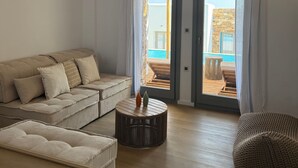 Uma sala de estar moderna com um sofá, uma mesa de centro redonda e vista para uma área externa com piscina.