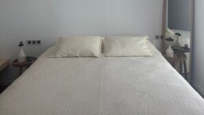 Quarto minimalista com uma cama grande, duas luminárias pendentes, uma mesa de cabeceira com um vaso e um espelho.