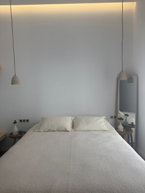 A minimalist bedroom with a large bed, two pendant lights, a bedside table with a vase, and a mirror. - 2-bedroom villa Odysseus (Antiparos)