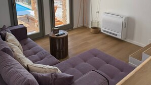 Una sala moderna con un sofá seccional grande, un televisor de pantalla plana en la pared, y vistas a una piscina y montañas a través de las ventanas.
