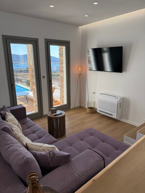 Una sala moderna con un sofá seccional grande, un televisor de pantalla plana en la pared, y vistas a una piscina y montañas a través de las ventanas.