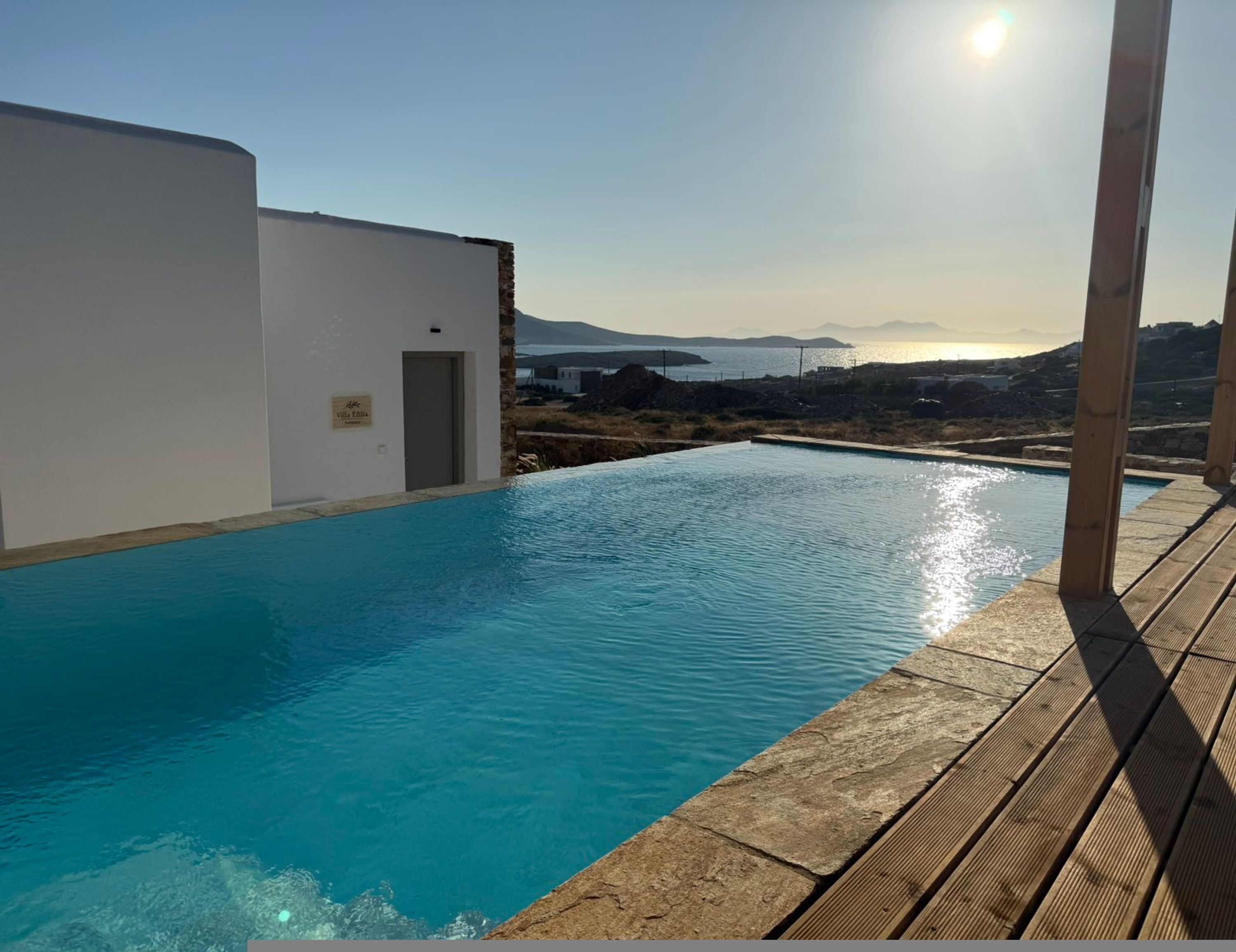 A swimming pool with a wooden deck and a white building with a door.