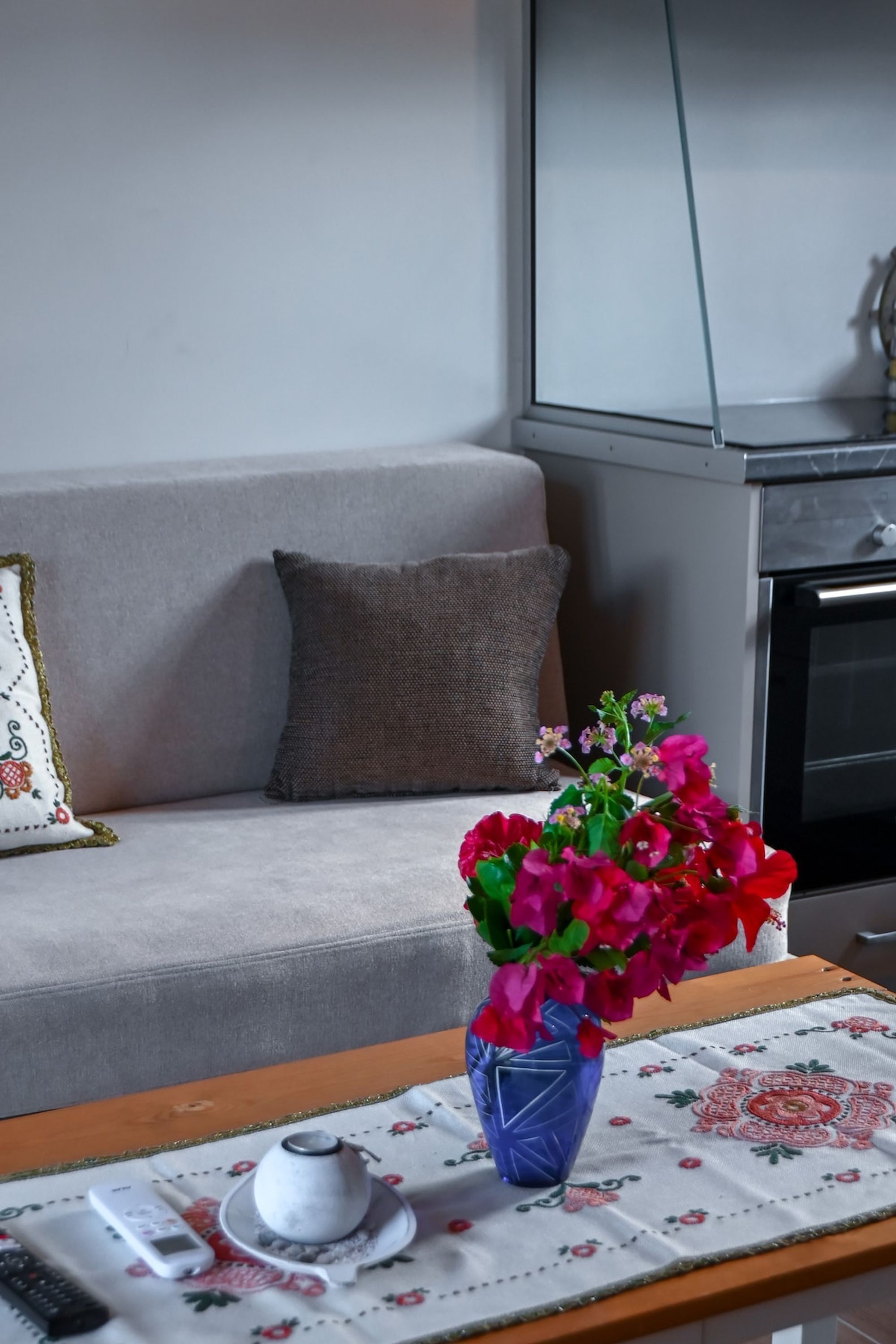 A living room with a sofa, a coffee table with a vase of flowers, a remote control, and a decorative plate.