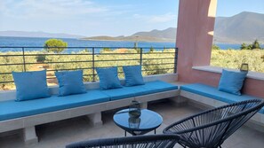 Un balcon doté d’un espace salon, d’une table et de chaises, offrant une vue sur la mer et les montagnes.