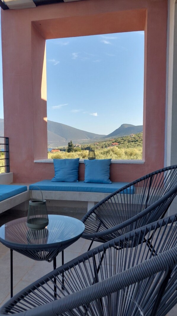 Un balcon avec vue sur les montagnes, un canapé avec des coussins et deux fauteuils.