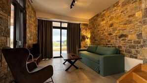 Uma sala de estar moderna com uma parede de pedra, um sofá verde, uma poltrona escura e uma mesa de centro de madeira.