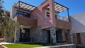 Um edifício moderno de dois andares com fachada de pedra, varanda e área de estar externa coberta.