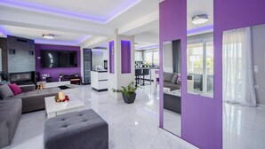 A modern living room with a flat-screen TV, a sofa, a coffee table, and a dining area with a kitchen in the background. - DimArist Residence in Zakynthos (Agios Kirikos)