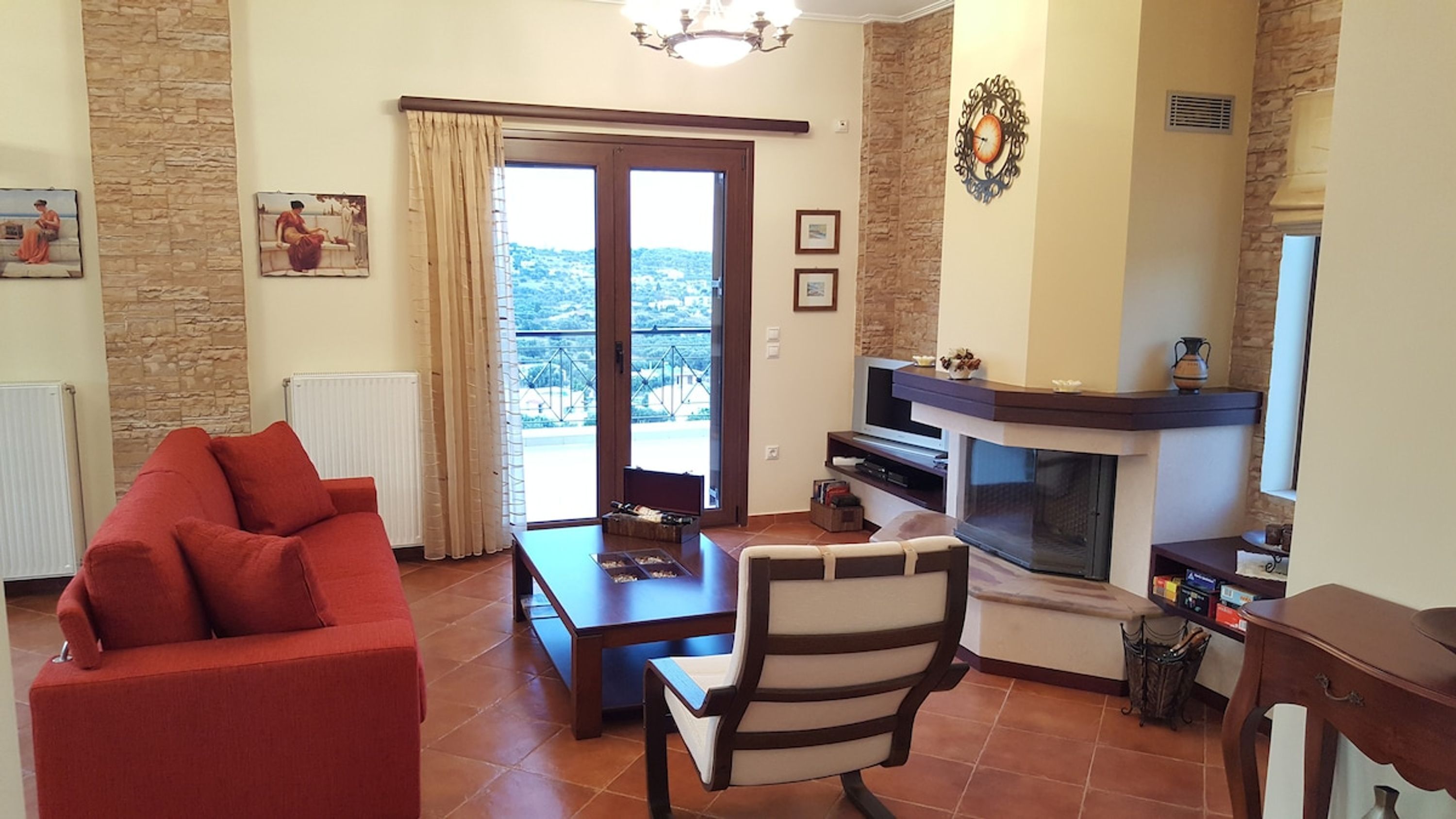 Ein Wohnzimmer mit einem roten Sofa, einem Holztisch, einem gestreiften Sessel, einem Kamin und einem Balkon mit Blick.