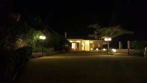 A well-lit, two-story house with a paved driveway leading to the entrance. - Villa Politimi at Aegina (Egina)