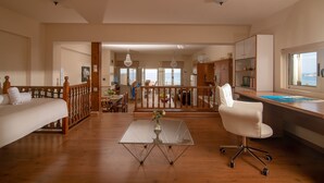 Una habitació àmplia amb terra de fusta, taula de vidre amb un ram, cadira blanca i escriptori amb un ordinador.