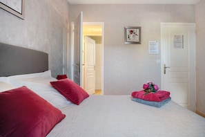 A hotel room with a bed, pillows, a nightstand, a framed picture, and a door with a notice.
