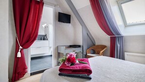 Ein Schlafzimmer mit einem Bett, einem Fernseher, einem kleinen Tisch mit einer Blume und einem Sessel.