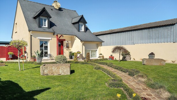 Ein Haus mit geneigtem Dach, einer Veranda und einem Garten mit einem Weg.