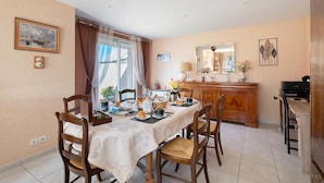 Un comedor con una mesa dispuesta para cuatro, sillas, un aparador de madera y un espejo en la pared.