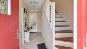 Una escalera con escalones de madera y barandas blancas que lleva a una plataforma con una puerta y una pequeña mesa con objetos encima.