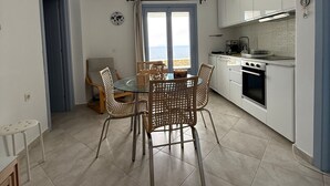 A compact kitchen with a dining area, featuring a round table with wicker chairs, a view through a window, and a built-in oven. - Iliada Suites Simousi Kythnos (Kithnos)