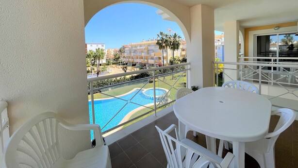 A balcony with a pool view, white furniture, and a clear sky. - Sunny 2 bedroom apartment in Denia 200m from the beach (Dénia)