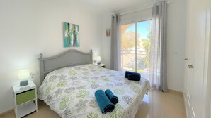 A bedroom with a bed, a nightstand, a lamp, a painting, and a view of the outside. - Sunny 2 bedroom apartment in Denia 200m from the beach (Dénia)