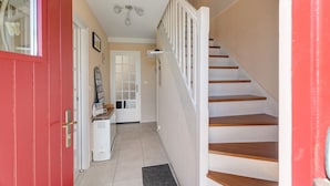 Una escalera con escalones de madera y barandas blancas que lleva a una plataforma con una puerta y una pequeña mesa con objetos encima.