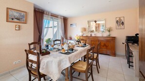 Un comedor con una mesa dispuesta para cuatro, sillas, un aparador de madera y un espejo en la pared.