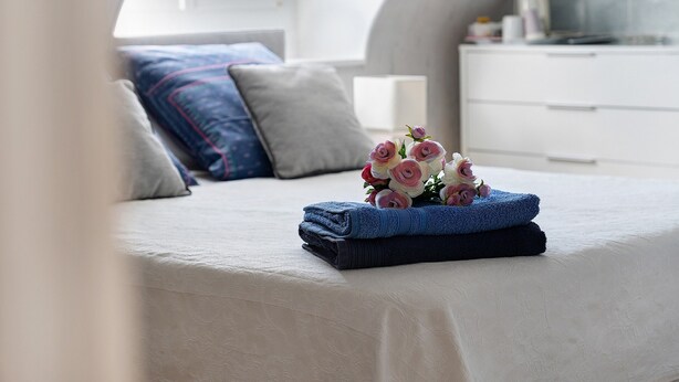 Una cama bien hecha con un ramo de flores, una toalla doblada y un aparador blanco en una habitación con techo curvo.