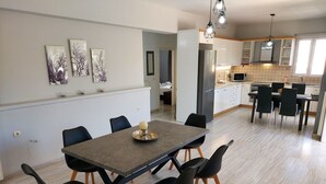 Una cocina moderna con armarios blancos, un refrigerador de acero inoxidable y una zona de comedor con una mesa de madera oscura y sillas negras.