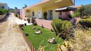 Una casa moderna de dos pisos con techo plano, un porche cubierto y un jardín cuidado con césped artificial y diversas macetas con plantas.