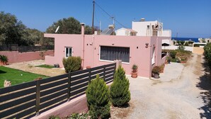Un edificio moderno de dos pisos con fachada rosa, patio cercado y plantas en macetas.