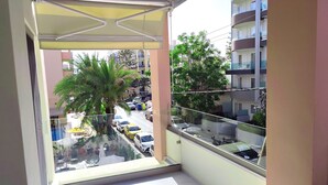 Uma varanda com vista para a rua, uma palmeira e um edifício com varandas.