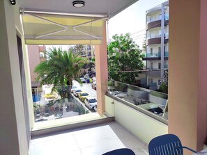 Ein Balkon mit Blick auf eine Straße, eine Palme und ein Gebäude mit Balkonen.