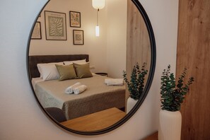 Ein Schlafzimmer mit einem Bett, Kissen, einem Nachttisch, einem Spiegel und gerahmten Kunstwerken an der Wand.