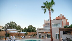 Une maison moderne à deux étages, dotée d’une piscine, de chaises longues et de parasols.