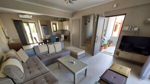 A modern living room with a sofa, coffee table, and a TV. There is a kitchen area with cabinets and a refrigerator. - Rethymno Suburb Maisonette (Rethimno)