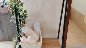 Una stanza con un appendiabiti in metallo nero contenente grucce di legno, un cesto di vimini con asciugamani piegati e una pianta in vaso con foglie variegate.