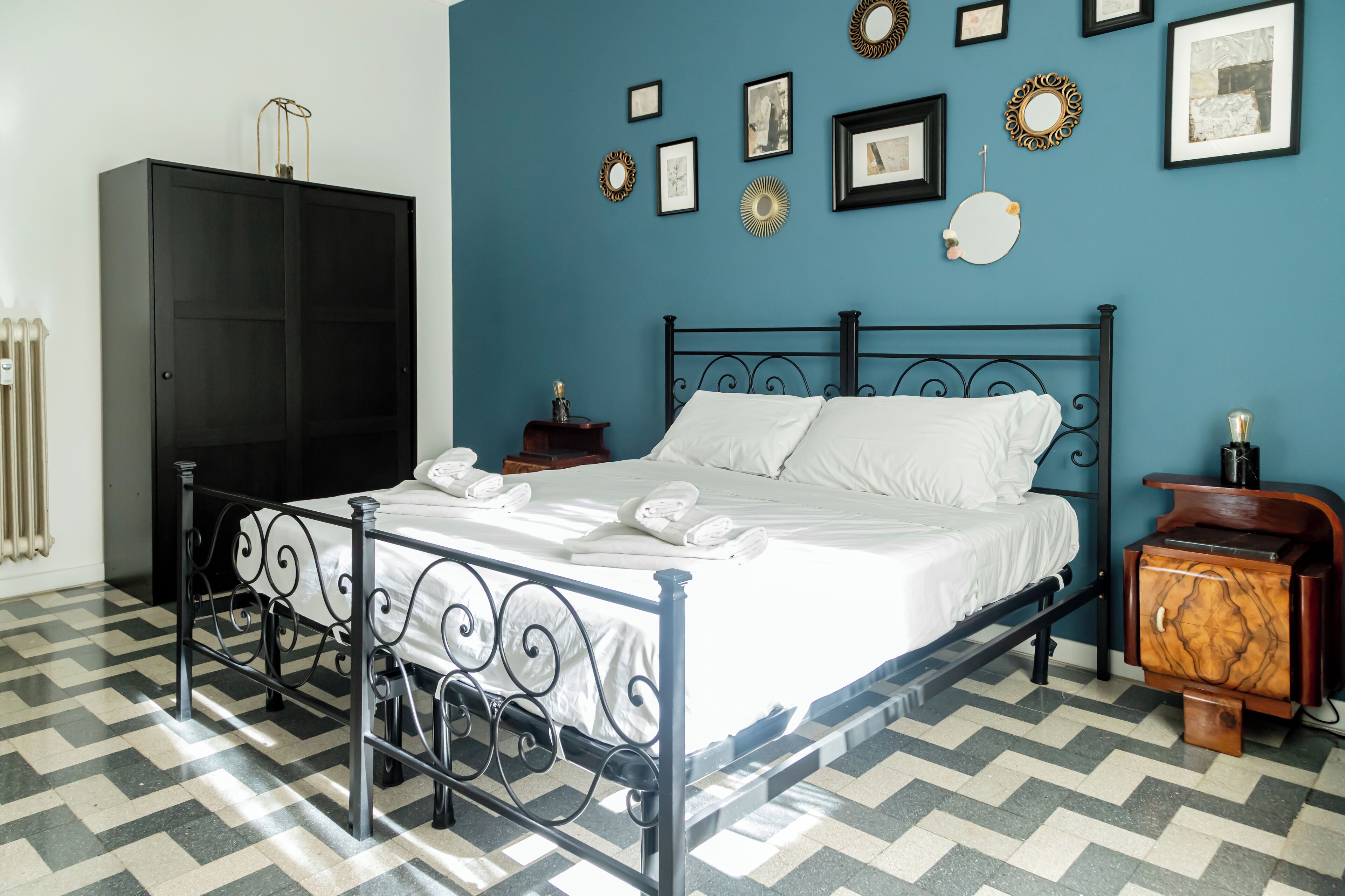 A bedroom with a bed, wardrobe, and a wall decorated with framed pictures.