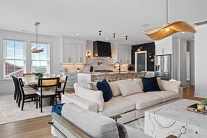 A modern kitchen with white cabinets, a large island, and a dining area with a sofa and chairs. - Oceanfront 6BR West Side Duplex w/ Pool, Elevator & Game Room (Emerald Isle)