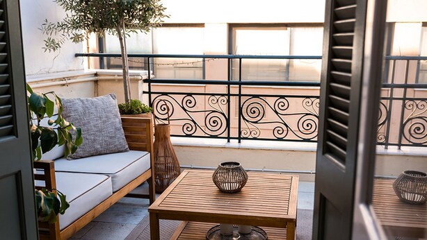 Een balkon met een houten bank, een bijzettafeltje en decoratieve objecten.