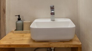 Kylpyhuone, jossa on valkoinen pesuallas, peili, saippua-annostelija ja valaisin.