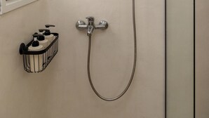 Kylpyhuone, jossa on lasinen suihkuseinä, käsisuihku, seinään asennettu hana ja saippua-annostelimen hylly.