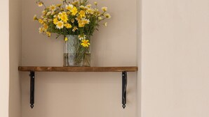 Een kitchenette met een koffiezetapparaat, een mand met snacks en een bloemenvaas op een plank.