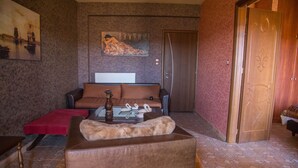 Een woonkamer met een bruine bank, een rode poef, een salontafel met decoratieve objecten en een schilderij aan de muur.