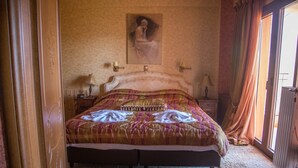 Een slaapkamer met een groot bed, een nachtkastje, een lamp en een schilderij aan de muur.